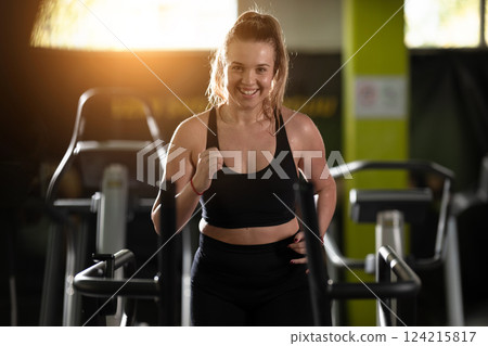 Woman Running on Treadmill in Gym.A fit woman wearing a purple sports outfit is running on a treadmill in a gym. She has a focused yet relaxed expression, with gym equipment and a warm light in the 124215817