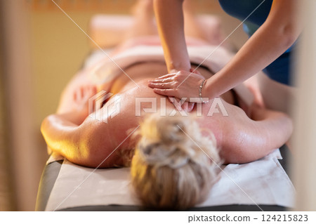 Relaxing Back Massage in a Spa Setting. A professional massage therapist in a blue uniform provides a relaxing back massage to a client lying on a massage table. Relaxing Back Massage in a Spa Setting. A professional massage therapist in a blue uniform provides a relaxing back massage to a client lying on a massage table. 124215823