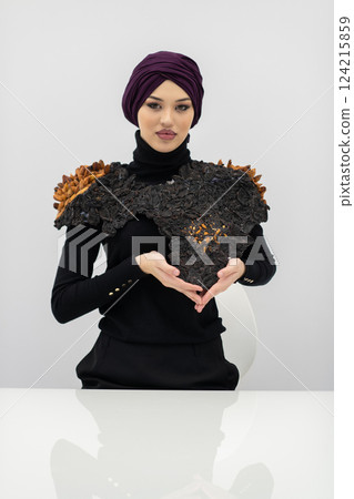 A stylish Muslim woman in a hijab presents her innovative handmade fashion accessory crafted from dried plums in a professional studio. 124215859