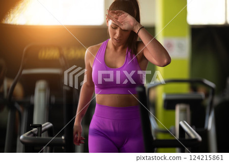 Woman Running on Treadmill in Gym.A fit woman wearing a purple sports outfit is running on a treadmill in a gym. She has a focused yet relaxed expression, with gym equipment and a warm light in the 124215861