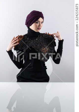 A stylish Muslim woman in a hijab presents her innovative handmade fashion accessory crafted from dried plums in a professional studio. 124215873