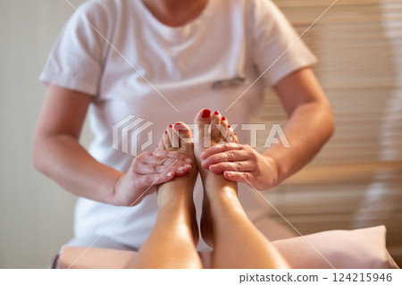 Foot Massage Therapy in a Relaxing Spa Setting. A professional massage therapist in a white uniform provides a soothing foot massage to a client in a calm and serene spa environment Foot Massage Therapy in a Relaxing Spa Setting. A professional massage therapist in a white uniform provides a soothing foot massage to a client in a calm and serene spa environment 124215946