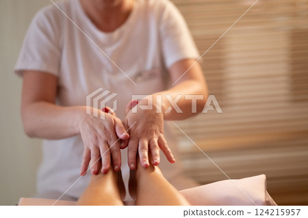 Foot Massage Therapy in a Relaxing Spa Setting. A professional massage therapist in a white uniform provides a soothing foot massage to a client in a calm and serene spa environment 124215957