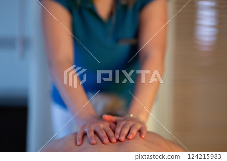 Relaxing Back Massage in a Spa Setting. A professional massage therapist in a blue uniform provides a relaxing back massage to a client lying on a massage table. Relaxing Back Massage in a Spa Setting. A professional massage therapist in a blue uniform provides a relaxing back massage to a client lying on a massage table. 124215983