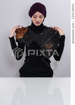 A stylish Muslim woman in a hijab presents her innovative handmade fashion accessory crafted from dried plums in a professional studio. 124216041