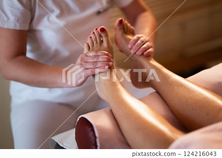 Foot Massage Therapy in a Relaxing Spa Setting. A professional massage therapist in a white uniform provides a soothing foot massage to a client in a calm and serene spa environment Foot Massage Therapy in a Relaxing Spa Setting. A professional massage therapist in a white uniform provides a soothing foot massage to a client in a calm and serene spa environment 124216043