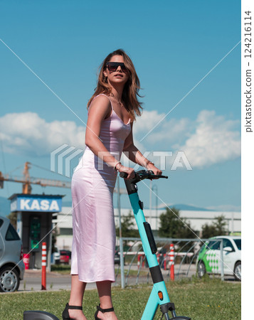 Elegant woman in a pink dress and sunglasses riding an electric scooter through the sunny city streets, embracing the freedom and style of a perfect urban adventure. Elegant woman in a pink dress and sunglasses riding an electric scooter through the sunny city streets, embracing the freedom and style of a perfect urban adventure. 124216114