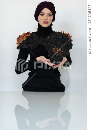 A stylish Muslim woman in a hijab presents her innovative handmade fashion accessory crafted from dried plums in a professional studio. A stylish Muslim woman in a hijab presents her innovative handmade fashion accessory crafted from dried plums in a professional studio. 124216145