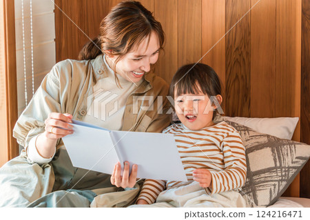 Mother reading a picture book to her daughter in the bedroom 124216471