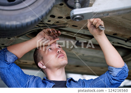 Car service, repair and mechanic working on car in the garage or workshop. Motor care, engineer and repairman standing under vehicle with wrench doing inspection, maintenance and fixing automobile 124216560