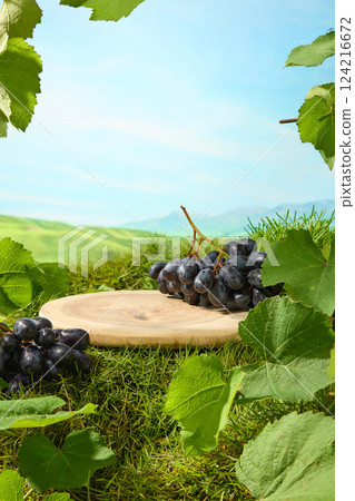 A bunch of grapes with deep purple berries placed on a round wooden tray with clearly visible wood grain in the middle of the garden. Close-up of a large-leaf grape branch with leaf grain. A bunch of grapes with deep purple berries placed on a round wooden tray with clearly visible wood grain in the middle of the garden. Close-up of a large-leaf grape branch with leaf grain. 124216672