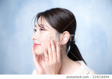 一位年輕女性的特寫，膚色光亮、清澈，注重皮膚護理，閉上雙眼，化著粉紅色妝容，背景為淺藍色背景 124216844