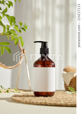 Front view mockup of a pump cosmetic bottle, no label used for design. Decorated with green leaves, straw mat and table mirror. Vegan cosmetics advertisement with minimalist concept. 124217115