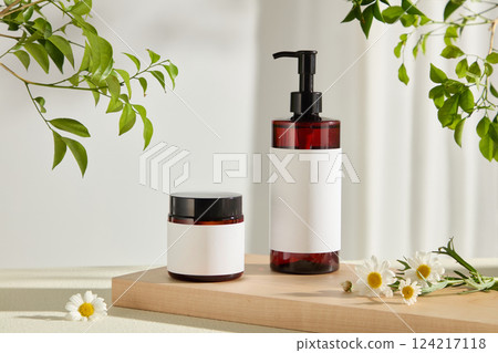 Plastic pump bottles and jars are placed on a rectangular wooden tray. White flowers are scattered around for decoration, green branches peek out into the photo. Use for cosmetic advertising. 124217118