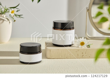 Close-up shot of two unlabeled jars on a stone pedestal, decorated with cute little flowers. The vase behind creates a highlight for the photo. Eco product presentation mockup. Advertising photo 124217129