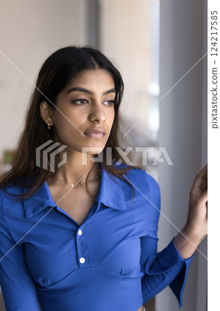 Indian woman standing indoors with thoughtful expression look into distance Indian woman standing indoors with thoughtful expression look into distance 124217585