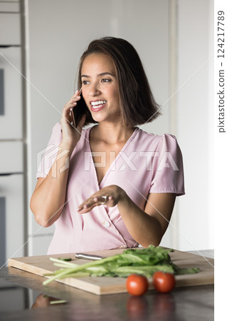 Young woman talking on her smartphone in kitchen at home 124217789