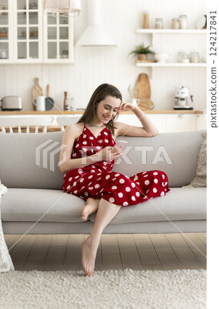 Smiling young girl sit on sofa text message on phone Smiling young girl sit on sofa text message on phone 124217841