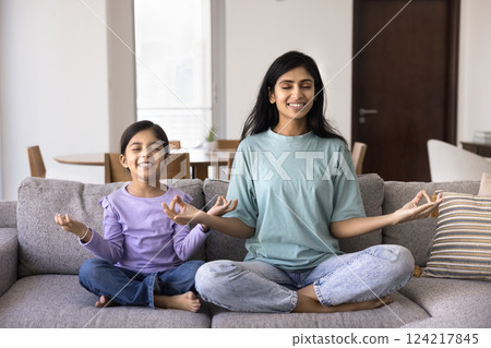 Mother and daughter do meditation practice on sofa 124217845