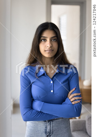 Serious young Indian woman standing indoor with arms crossed 124217846