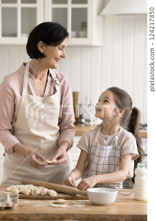 Happy smiling old grandmother little granddaughter making dumplings in kitchen 124217850