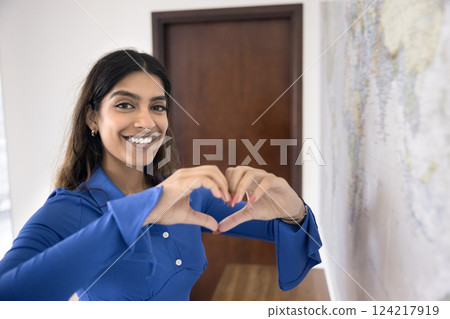 Woman forms heart with hands while standing near world map Woman forms heart with hands while standing near world map 124217919