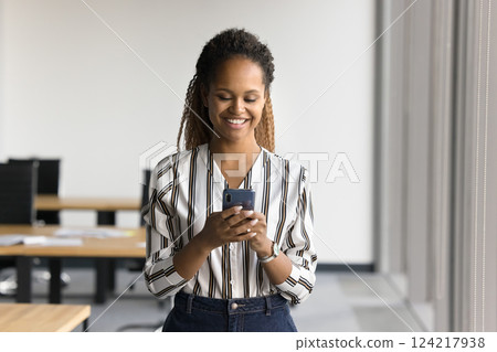Attractive African female employee using modern smartphone in coworking office Attractive African female employee using modern smartphone in coworking office 124217938
