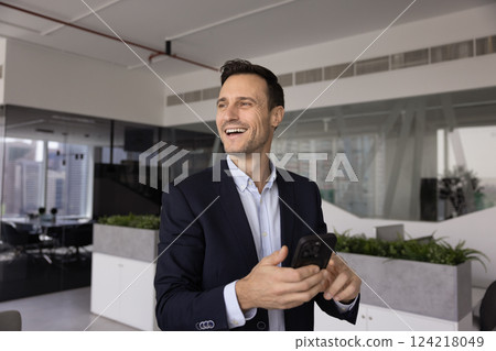 Happy mid adult Hispanic businessman using cellphone, standing in office Happy mid adult Hispanic businessman using cellphone, standing in office 124218049