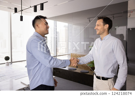 Happy male multiethnic business partners shaking hands in office Happy male multiethnic business partners shaking hands in office 124218074