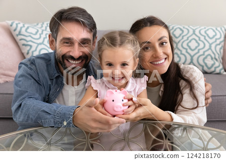 Happy mom and dad hugging little daughter kid holding piggybank Happy mom and dad hugging little daughter kid holding piggybank 124218170