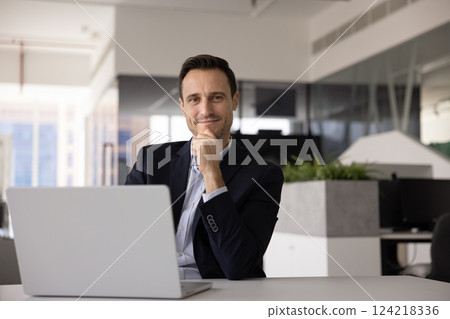 Happy confident Latin businessman posing at workplace with laptop Happy confident Latin businessman posing at workplace with laptop 124218336