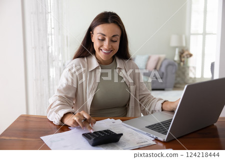 Positive young freelance accountant woman typing on calculator at home 124218444