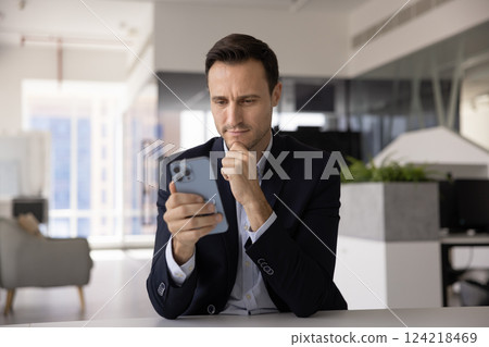 Focused pensive Latin CEO man examining content on mobile phone 124218469