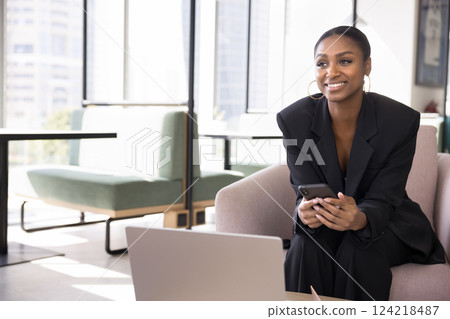 Young woman sitting in office lounge area with smartphone 124218487