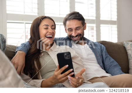 Cheerful Hispanic couple watching funny content on mobile phone 124218519