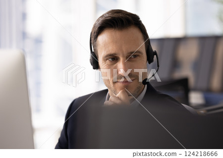 Positive thoughtful contact center manager in headset sitting at computer 124218666