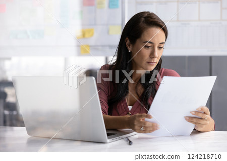 Latin business professional woman reading paper financial report Latin business professional woman reading paper financial report 124218710
