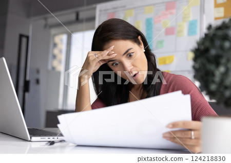 Surprised businesswoman reading paper financial report in office 124218830
