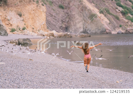 A woman is running on a beach with a flock of birds flying in the background. The scene is peaceful and serene, with the woman enjoying the beauty of nature. 124219535