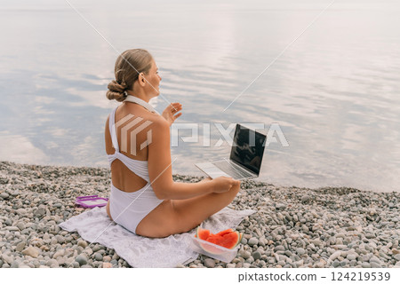 A woman is sitting on the beach with a laptop open in front of her. She is wearing a white bikini and has a pink headband on. Concept of relaxation and leisure. A woman is sitting on the beach with a laptop open in front of her. She is wearing a white bikini and has a pink headband on. Concept of relaxation and leisure. 124219539