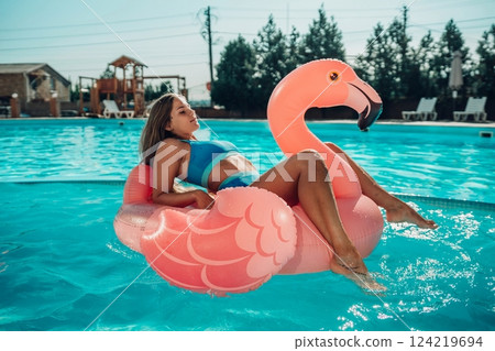 A woman is floating on a pink flamingo float in a pool. The scene is relaxed and fun, with the woman enjoying her time in the water. A woman is floating on a pink flamingo float in a pool. The scene is relaxed and fun, with the woman enjoying her time in the water. 124219694