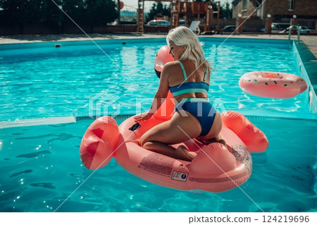 A woman is sitting on a pink inflatable raft in a swimming pool 124219696