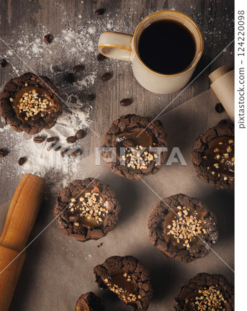 Freshly baked muffins on baking paper, coffee mug, rolling pin, flour and coffee beans on a table, top view, vertical image. 124220098