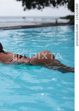 A woman enjoying swimming in a beautifully clear pool located by the vast ocean shores 124221689