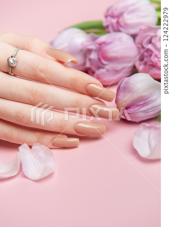 Woman showing stylish nude manicure near purple tulips on pink background 124222979