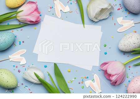 Easter eggs and tulips framing blank greeting card on pastel blue background 124222990