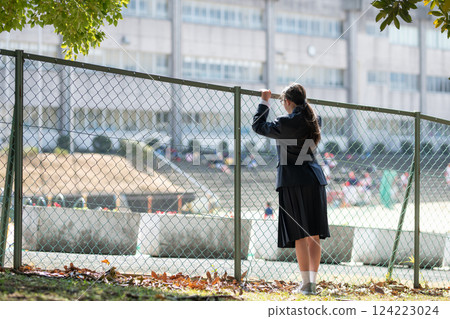 A female student looking at the school through the fence A female student looking at the school through the fence 124223024