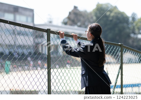 一名女學生透過柵欄望向學校 一名女學生透過柵欄望向學校 124223025