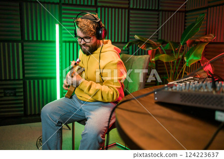 Male singer recording songs by using a studio microphone and and playing guitar in a music recording studio. Performance and show in the music business, streaming and recording music. 124223637