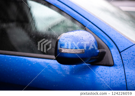 Close-up of a blue car side mirror with water droplets after rain, reflecting urban environment. Close-up of a blue car side mirror with water droplets after rain, reflecting urban environment. 124226059